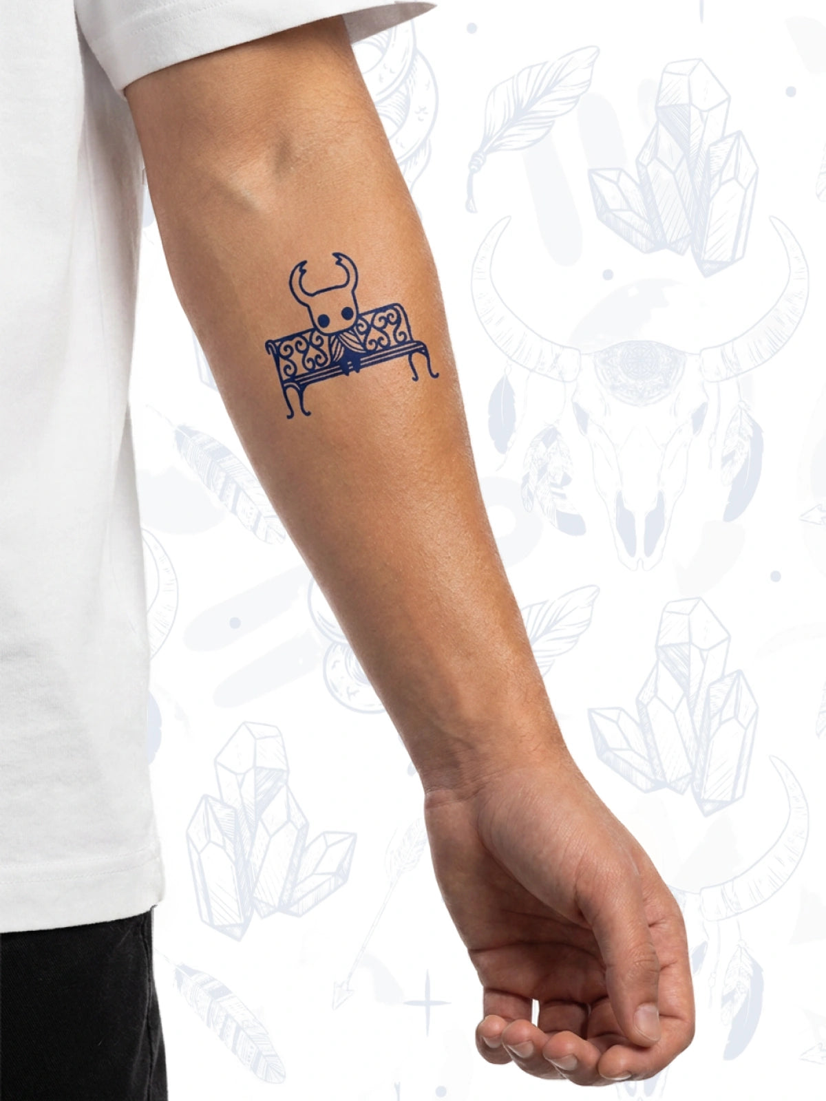 A temporary tattoo applied to a person's inner forearm, featuring a dark blue bull sitting on an ornate bench. The person is wearing a white t-shirt, and the background is white with faint gray decorative illustrations.