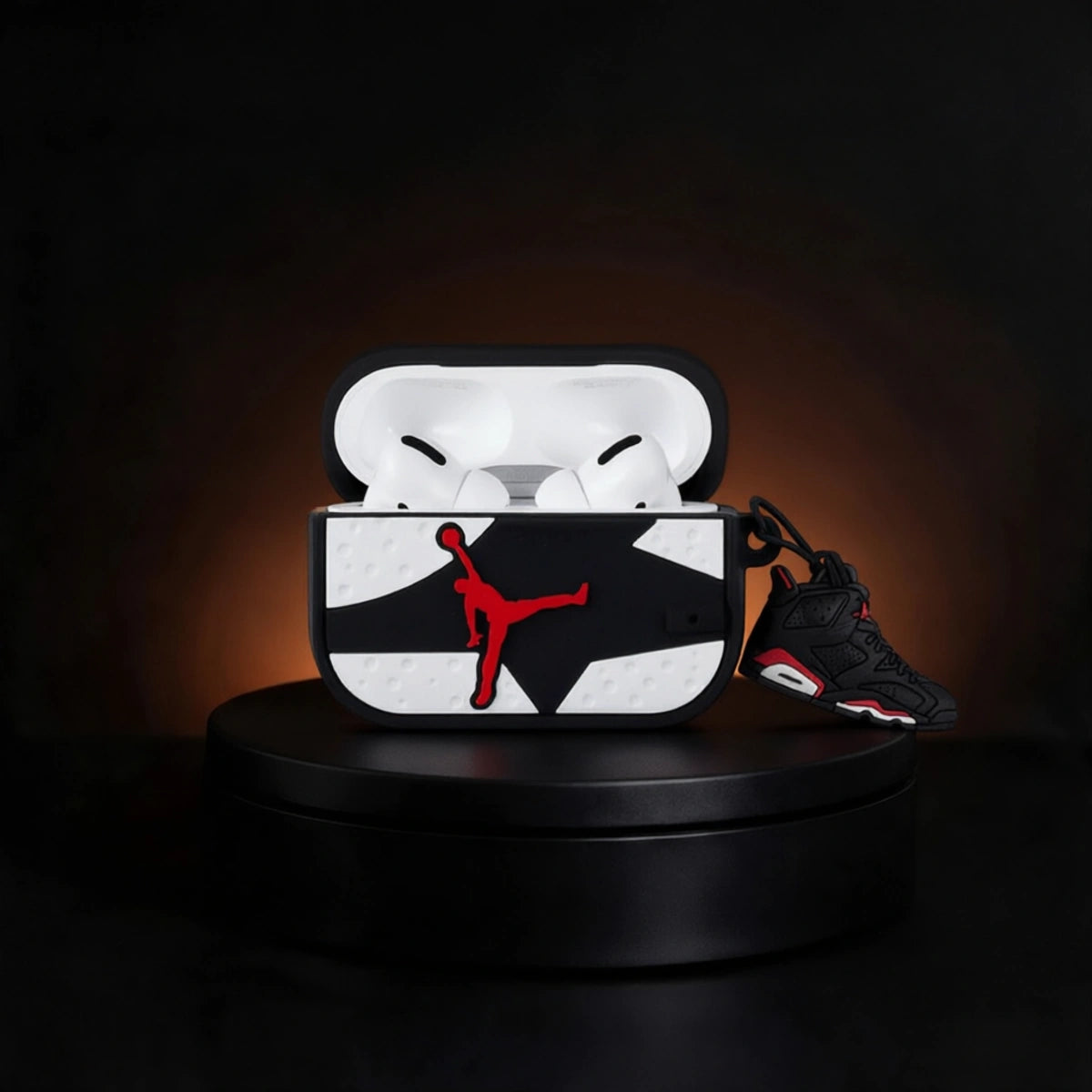 A custom AirPods case featuring a black and white geometric pattern with a red Jordan logo, shown open with white AirPods inside and a black and red Air Jordan sneaker resting beside it on a black display pedestal.