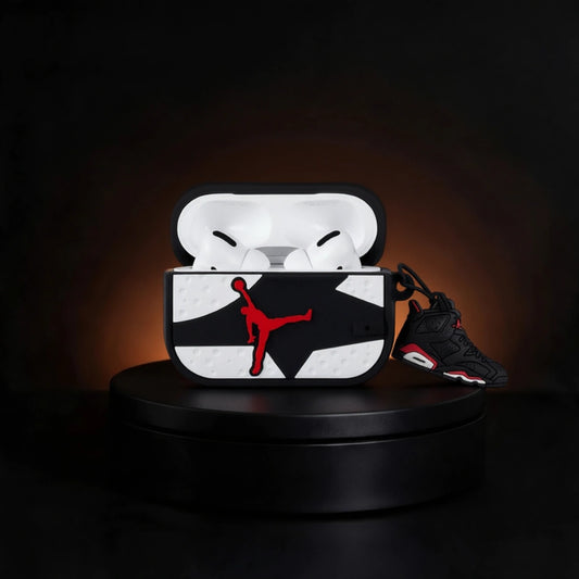 A custom AirPods case featuring a black and white geometric pattern with a red Jordan logo, shown open with white AirPods inside and a black and red Air Jordan sneaker resting beside it on a black display pedestal.