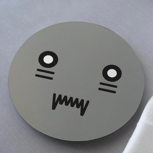Round gray coaster with a cartoon face design on a light gray background