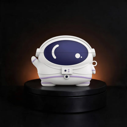 A white astronaut-shaped case for airpods and buds,  with a dark blue visor and subtle purple accents, displayed on a black circular pedestal against a dark background with warm light glow.