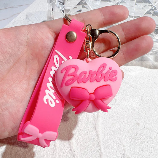 Pink 'Barbie' keychain with a heart-shaped design held in a hand against a textured white background.