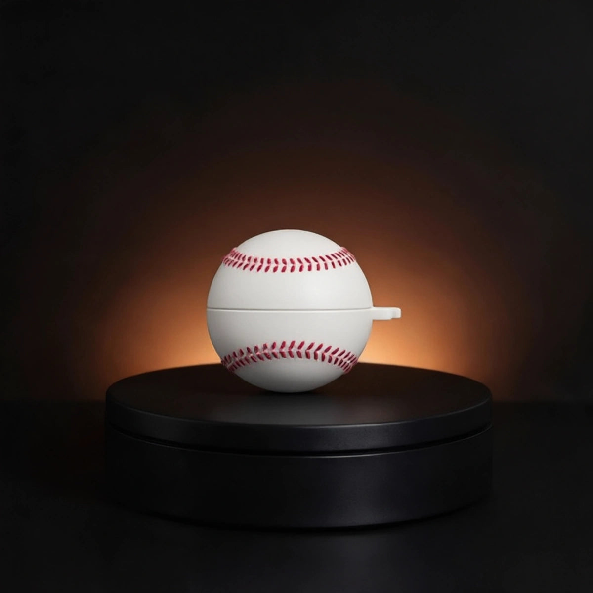 A white baseball-shaped galaxy buds2 case with red stitching sits centered on a round black pedestal against a dark background with a warm spotlight glow.