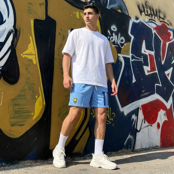 Person wearing a white t-shirt and blue shorts standing in front of a graffiti wall.