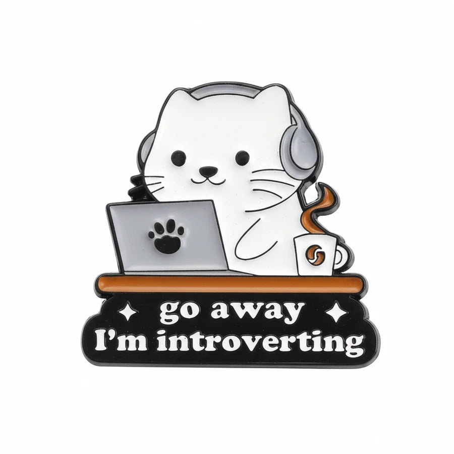 Enamel pin with a cat wearing headphones, using a laptop, and a coffee cup with text 'go away I'm introverting' on a white background.