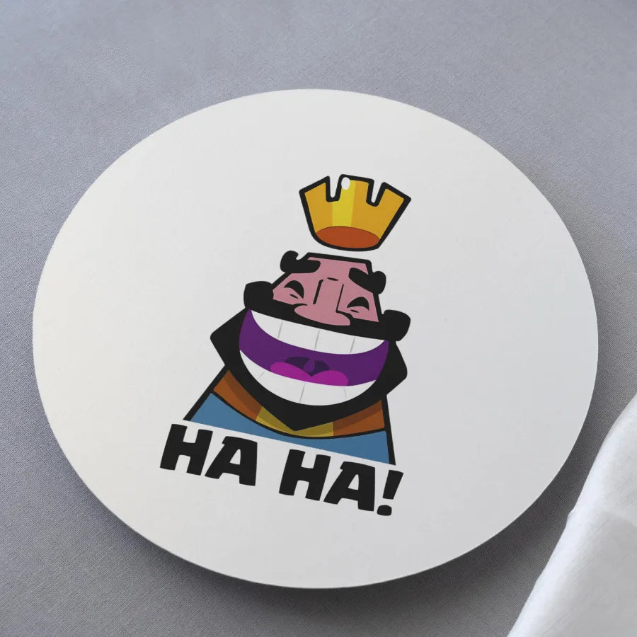 Round white coaster with a colorful illustration of a character wearing a crown and rainbow outfit, with 'HA HA!' text on a gray background.