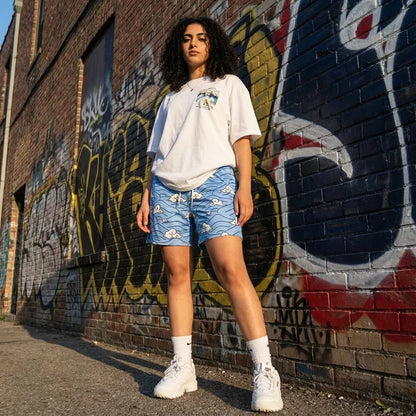 Person wearing a white t-shirt and blue shorts with floral pattern in front of a graffiti-covered wall.