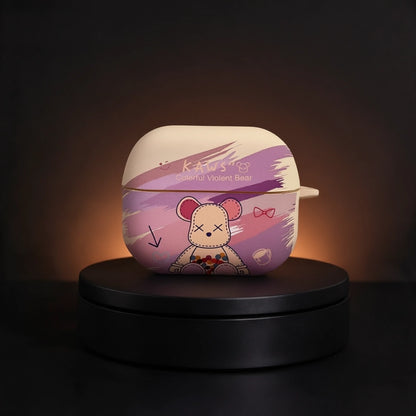 A protective AirPods case with a cartoon bear design, displayed on a black circular pedestal against a dark background. The case features a cream-colored top half and a purple bottom half with a cartoon bear illustration and the text 'Kaws' and 'Animal Violence Bear'.