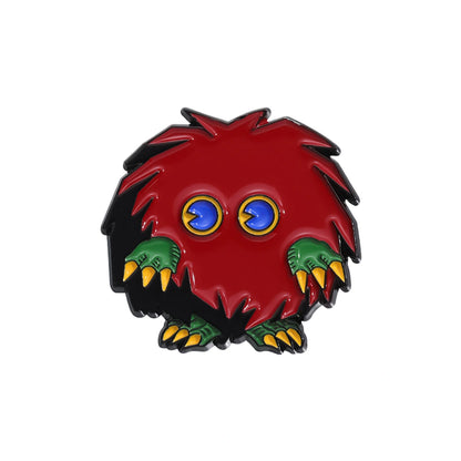 A small monster-shaped enamel pin featuring a red body with black spiky hair, blue eyes, green claws, and yellow accents, shown on a plain white background.