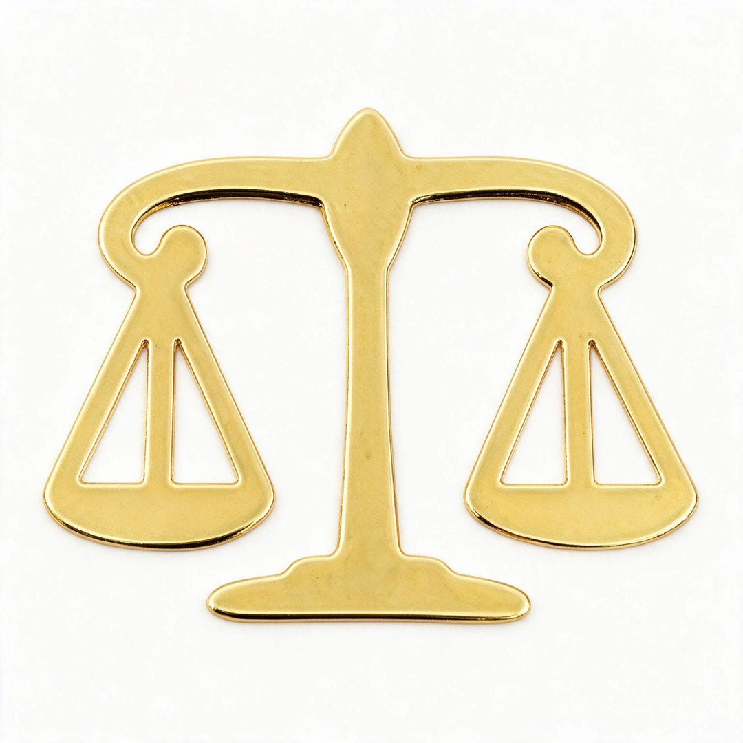 A polished gold-colored metal scale of justice pendant or emblem, shown against a plain white background.