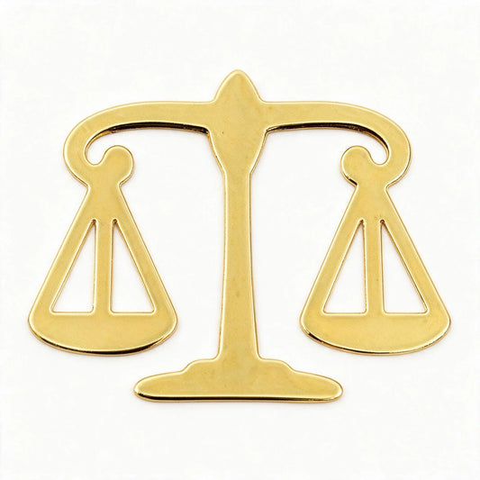 A polished gold-colored metal scale of justice pendant or emblem, shown against a plain white background.