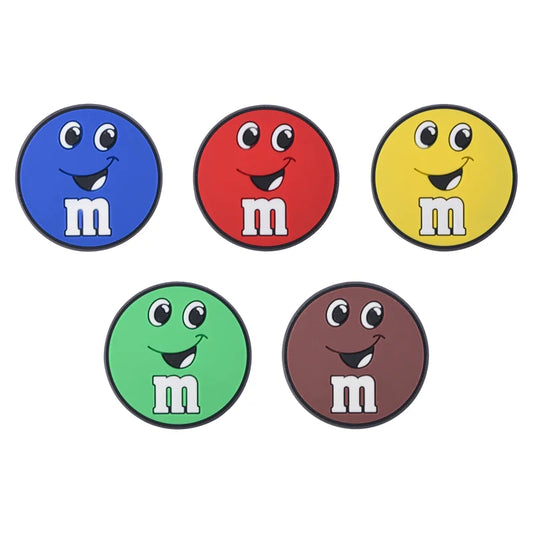 Five M&M character croc charms in blue, red, yellow, green, and brown on a white background.