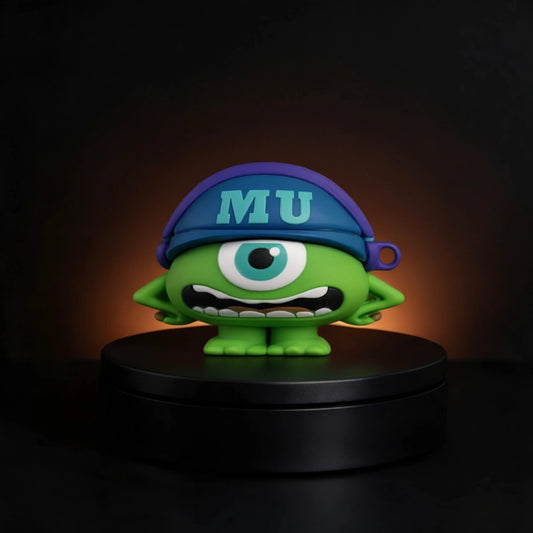 A green one-eyed cartoon character mike wazowski from monsters inc airpods and buds case figurine wearing a blue cap with 'MU' in light blue, standing on a black circular base against a dark background with a warm glow.