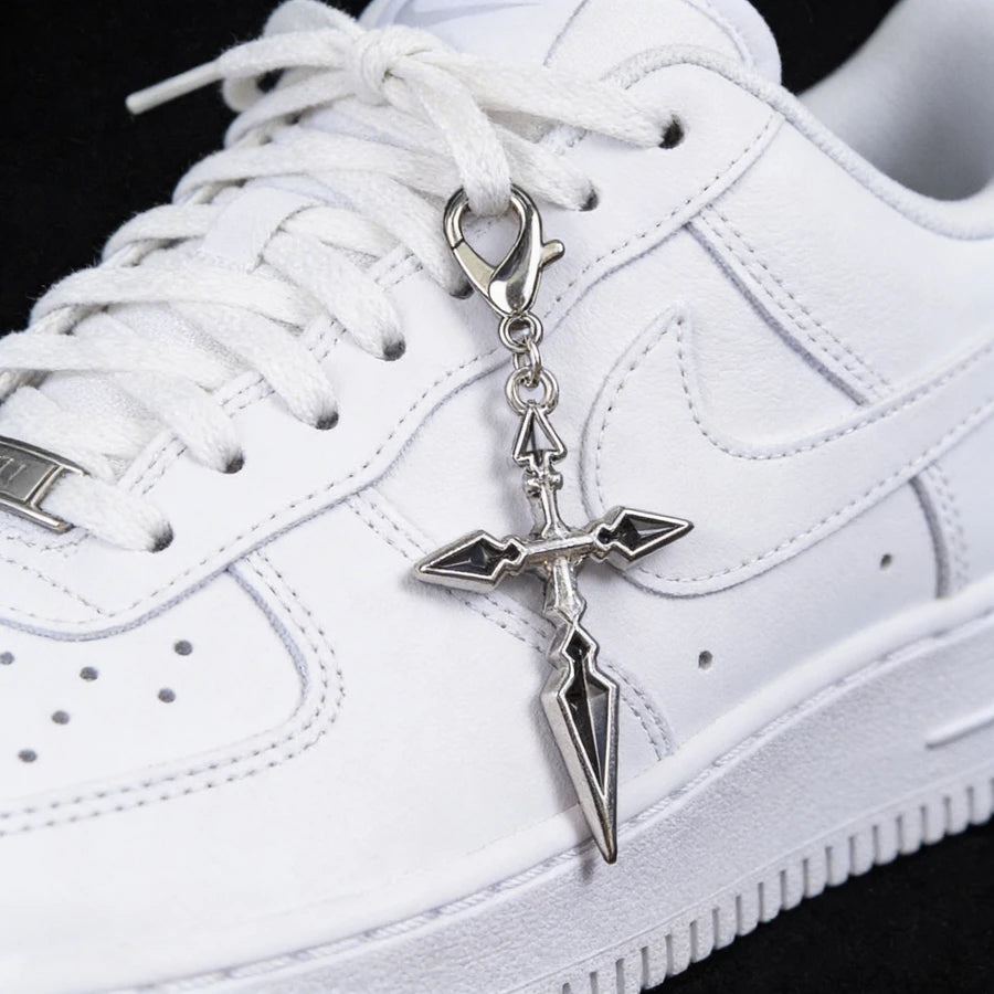 White sneaker with a silver cross-shaped keychain on a black background
