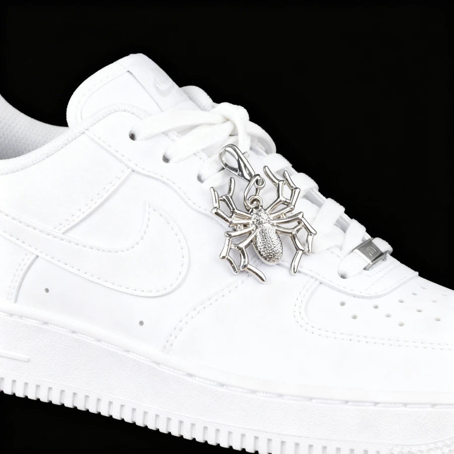 White sneaker with a silver spider charm on a black background