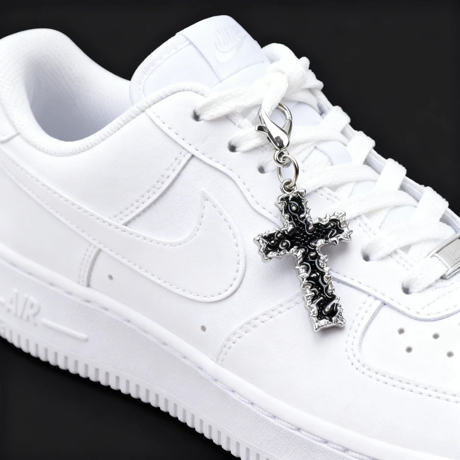 White sneaker with a black cross charm on a black background