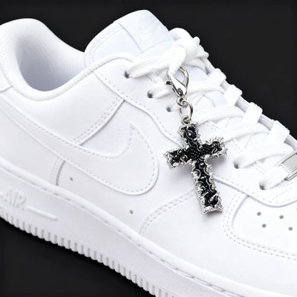 White sneaker with a black cross charm on a black background