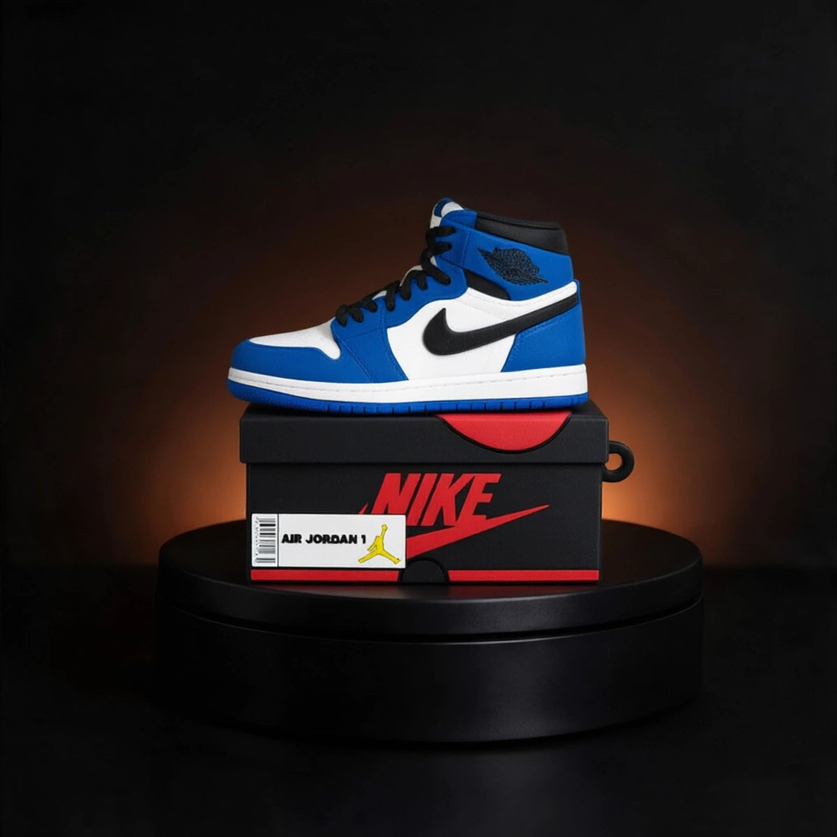 A blue, white, and black Nike Air Jordan 1 high-top sneaker case for apple airpods  sits on top of a black Nike shoebox with a red logo, displayed on a black circular pedestal against a dark background with a warm spotlight.
