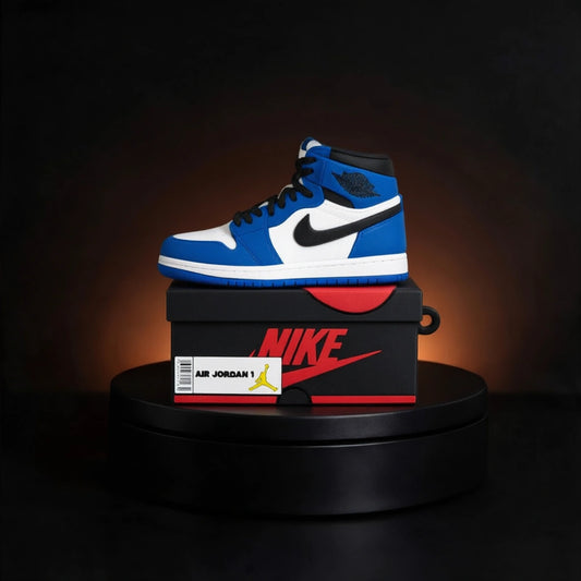 A blue, white, and black Nike Air Jordan 1 high-top sneaker case for apple airpods  sits on top of a black Nike shoebox with a red logo, displayed on a black circular pedestal against a dark background with a warm spotlight.