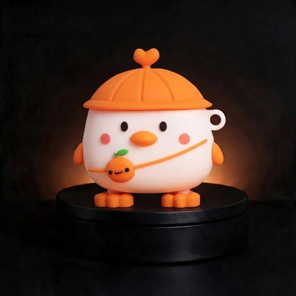 A cute cartoon air pocket case shaped like a white bird or duckling wearing an orange cap and holding an orange, displayed on a black circular base against a dark background.