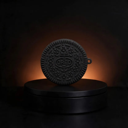 A black silicone case designed to look like an Oreo cookie, featuring the embossed OREO logo in the center, displayed on a black circular pedestal against a dark background with a warm orange glow.