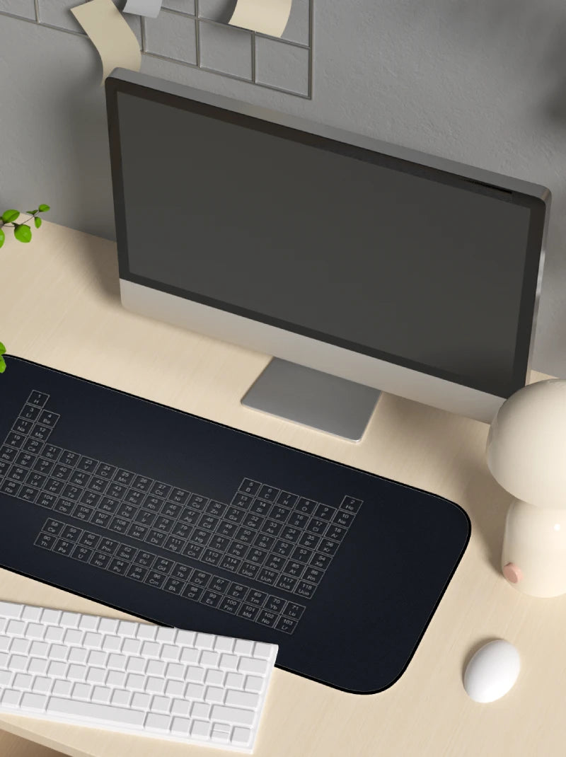 Computer setup with a monitor, keyboard, mouse, and a mouse pad with a periodic table on a desk.