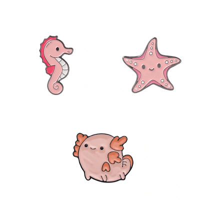 Three cute cartoon sea-themed enamel pins on a plain white background: a pink seahorse, a pink starfish, and a round pink axolotl.