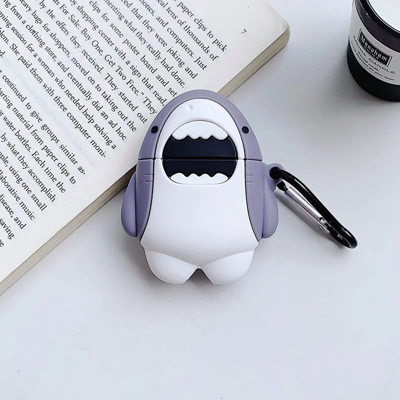 Shark-shaped air pod case on a white surface with a book and bottle in the background