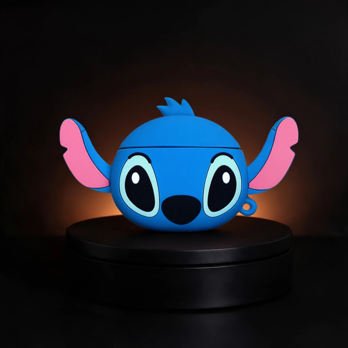 A blue cartoon character stitch airpods and galaxy buds case with pink inner ears and large white eyes, displayed on a black circular pedestal against a dark background.