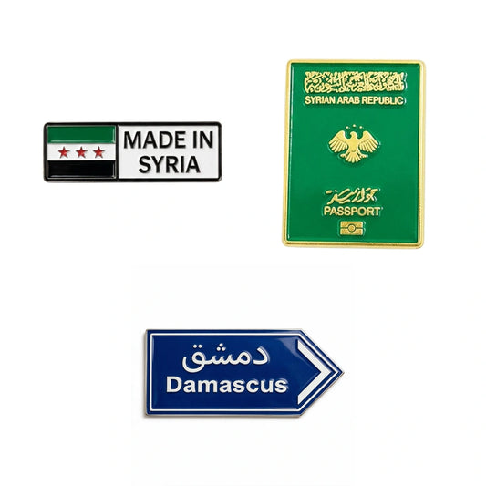 Three Syria-themed enamel phone stickers on a plain white background: a rectangular pin reading 'MADE IN SYRIA' with the Syrian flag, a green passport-style pin labeled 'SYRIAN ARAB REPUBLIC' and 'PASSPORT' with a gold emblem, and a blue directional sign pin pointing right with Arabic text and 'Damascus'.