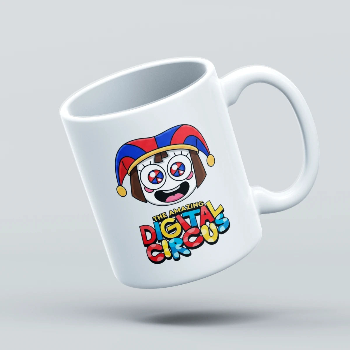 A white ceramic coffee mug with a colorful cartoon jester face and the text 'The Amazing Digital Circus' printed on it, shown floating against a light gray background.
