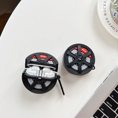 Black and red earbud case with white earbuds on a light surface next to a laptop.