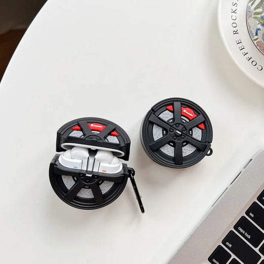 Black and red earbud case with white earbuds on a light surface next to a laptop.